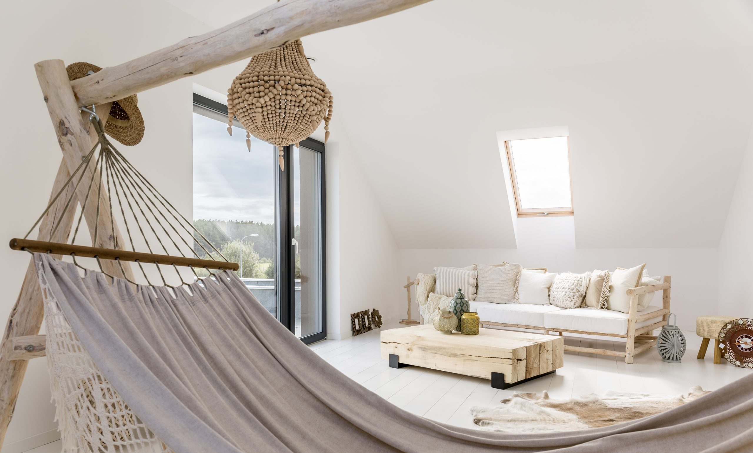 Grey handmade hammock standing in the white attic room with wooden sofa